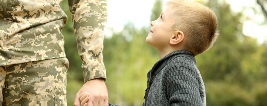 Young boy holds hands with soldier dad.