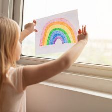 kid hanging rainbow in window during covid