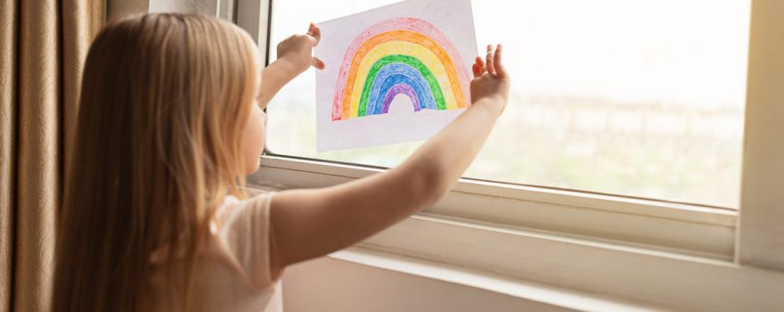 kid hanging rainbow in window during covid