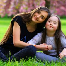 girl with special needs with another girl sitting in grass