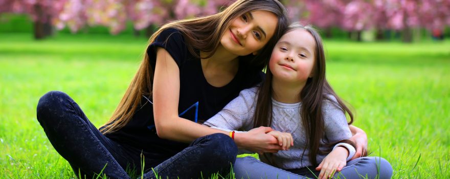 girl with special needs with another girl sitting in grass
