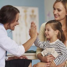 child giving pediatrician high-five while parent asks questions