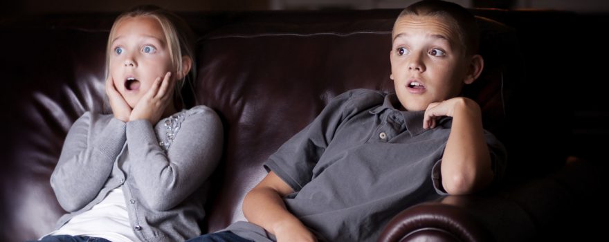 Boy and girl sitting on couch watching tv looking shocked