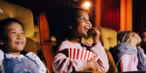 Kids eat popcorn and watch a movie at the movie theater