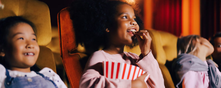 Kids eat popcorn and watch a movie at the movie theater