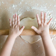 child's hands flattening dough with a rolling pin