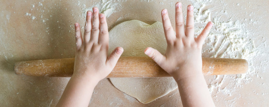 child's hands flattening dough with a rolling pin