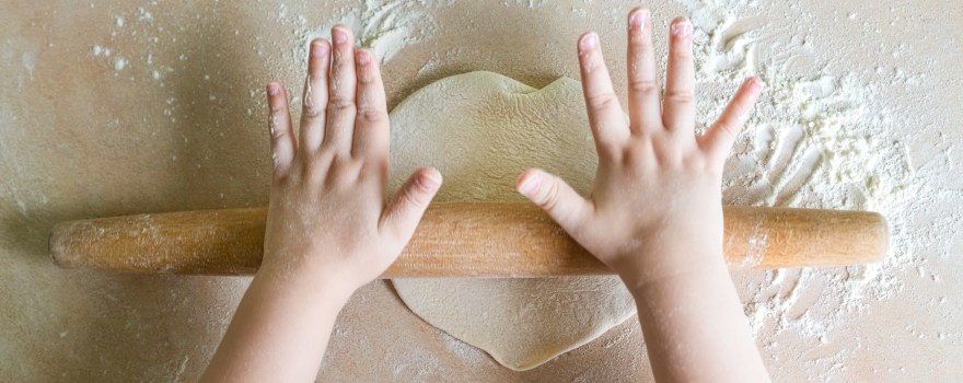 child's hands flattening dough with a rolling pin