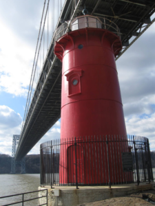 little red lighthouse on a clear day with a bridge above it