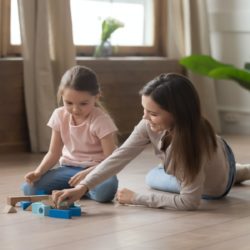 Happy mother and little daughter playing with toys together on wooden warm floor, smiling young mum and cute preschool girl having fun, spending time at home, underfloor heat, horizontal banner