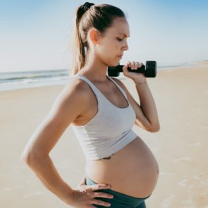Pregnant woman lifting a weight at the beach.