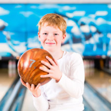 Child holding bowling ball at a bowling alley.