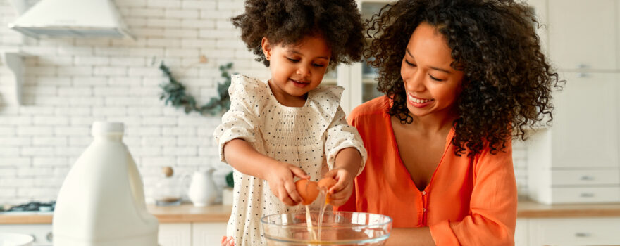 Parent and child preparing food together in a kitchen.