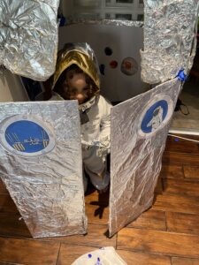 Little girl, whose mom is in a super mom contest, wearing an astronaut costume in her living room.