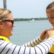 Mother putting life jacket on child. Wearing a life jacket is one of the most important boat safety tips for families and individuals.