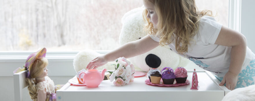 a little girl having a tea party with her doll, which shows one of many ways doll playing helps kids
