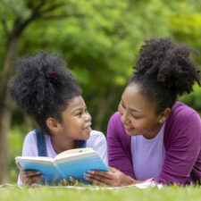 Mother and child on a lawn reading together. Reading is a way to fight summer learning loss.