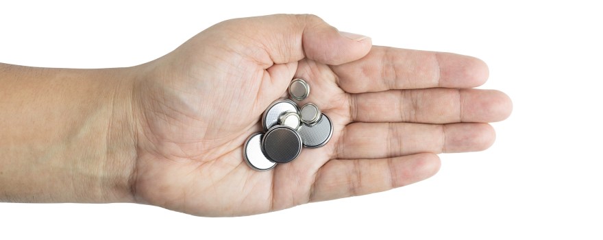 An adult human hand holding lithium coin batteries.