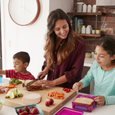 children and their mother preparing healthy school lunches in the kitchen at home