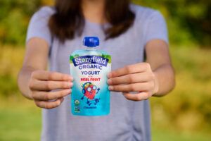 person holding a pouch with organic yogurt, which can be included when preparing healthy school lunches