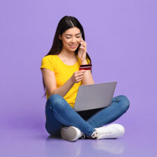a young girl holding a credit card and with a laptop, included in an article about talking to your teen about credit