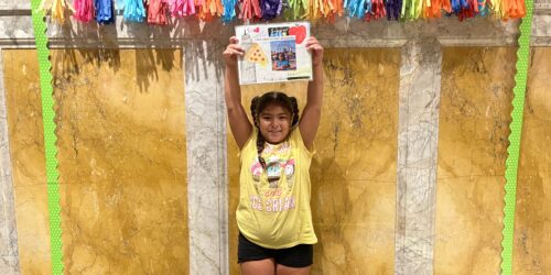 a little girl standing and holding up the story she wrote for a NYPL writing contest