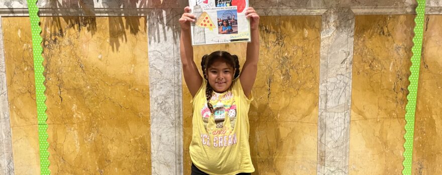 a little girl standing and holding up the story she wrote for a NYPL writing contest