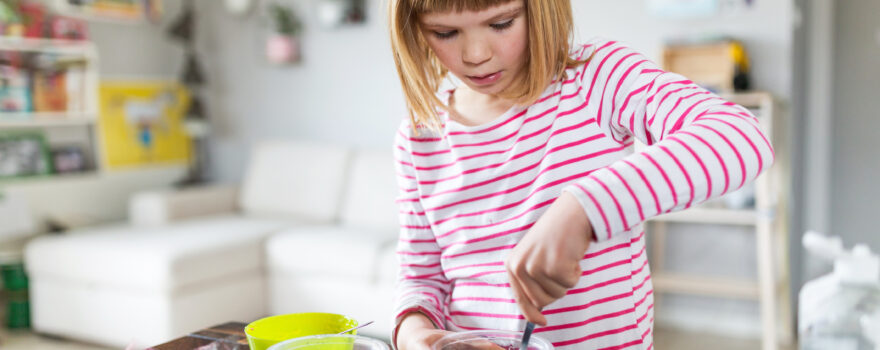 Little girl at home in her kitchen with bowls of different ingredients, showing how to make slime