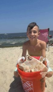 little boy at the beach on a sunny day collecting and disposing of litter, which he does on some NJ and Staten Island beaches