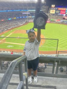 a little girl, who won a NYPL writing contest, standing in the bleachers of a baseball stadium holding a Yankees sign