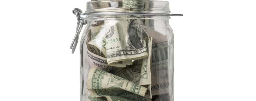 A jar for savings filled over the top with American coins and bills.