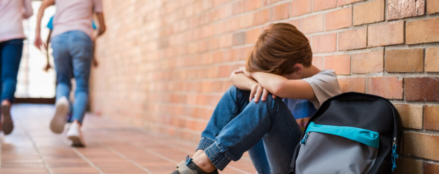 Young boy in school, looking withdrawn, which is one of several signs of bullying