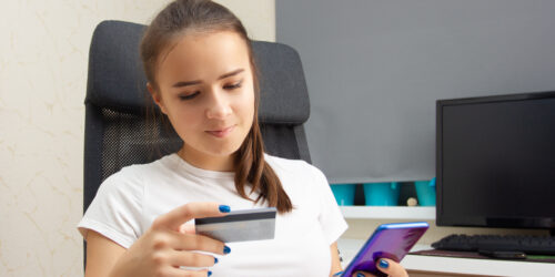 Teen girl at a desk social media spending with credit card and phone in hand